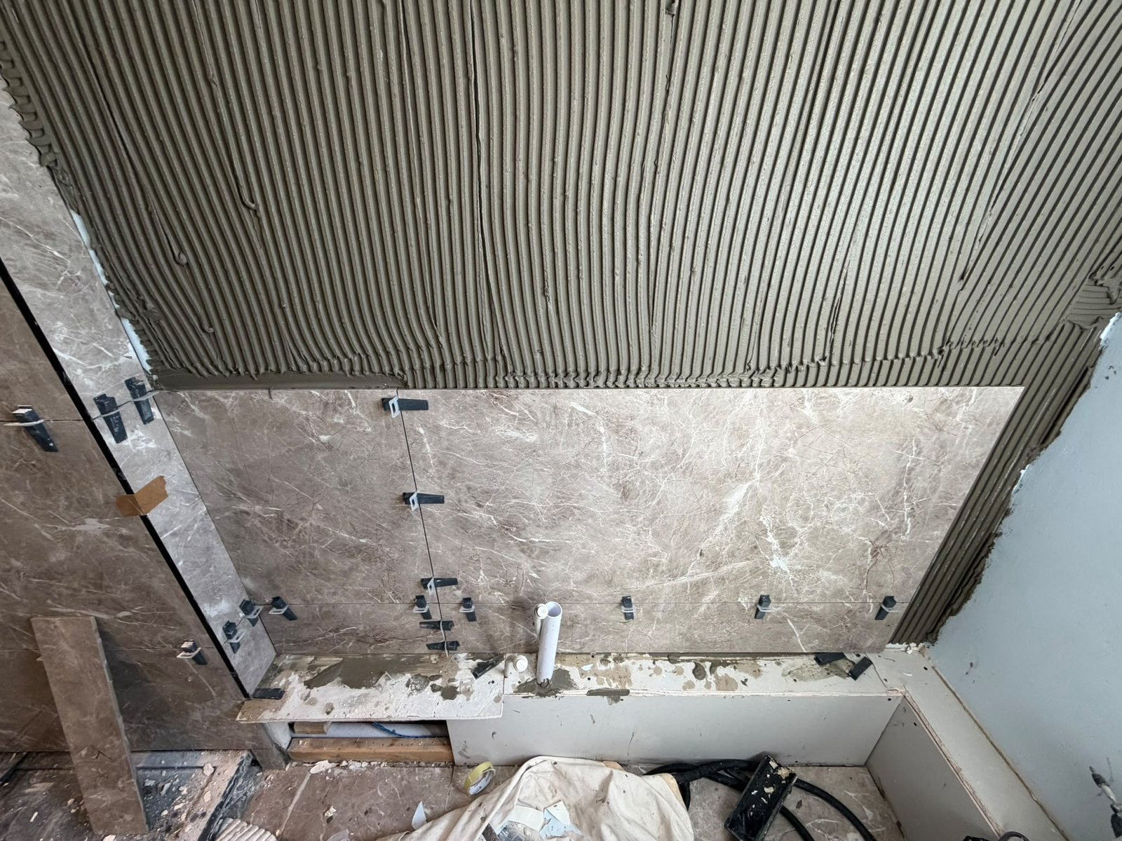 Large-format marble-effect wall tile being fixed in a shower