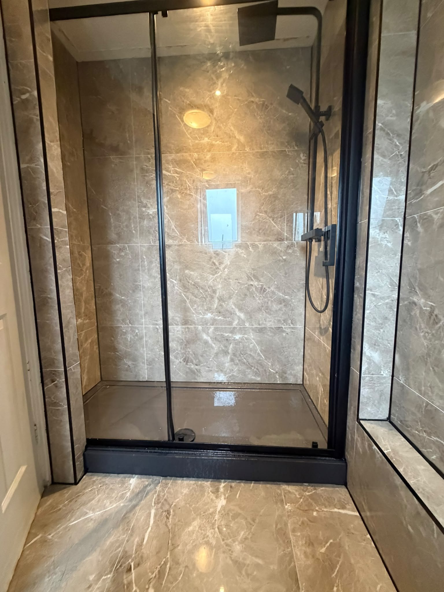 Marble-effect tiled shower room with glass screen by SN&J Construction